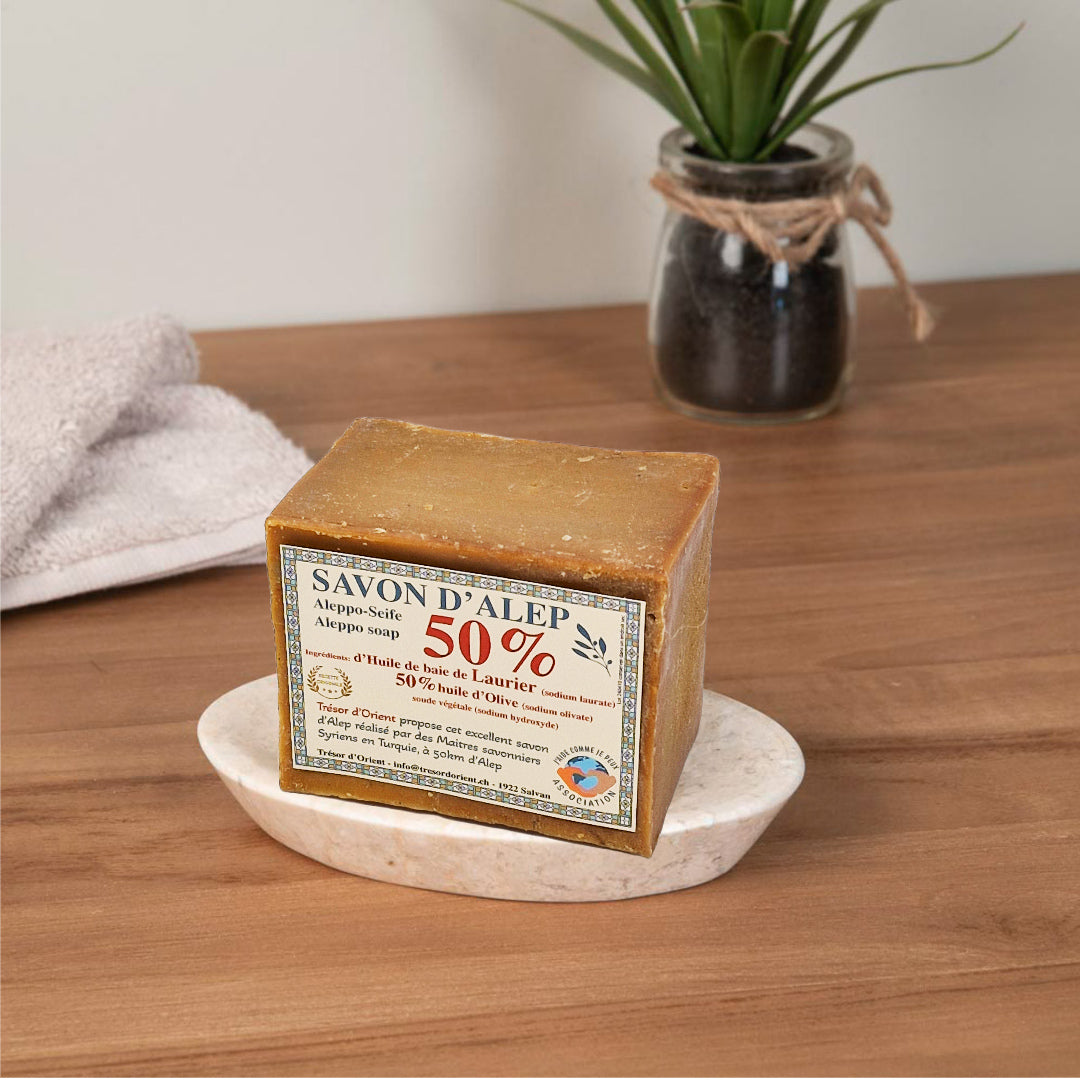 Savon d’Alep 50 % d’huile de laurier de Trésor d’Orient posé sur un porte-savon en bois clair, ambiance naturelle.